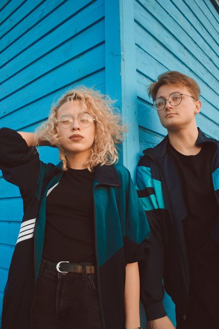 A trendy young couple posing in fashionable outerwear against a vibrant blue background, exuding modern style.