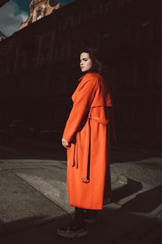 Stylish woman in a vibrant red coat posing on a city street by day.