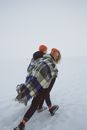 Couple walking on snow with warm plaid on shoulders