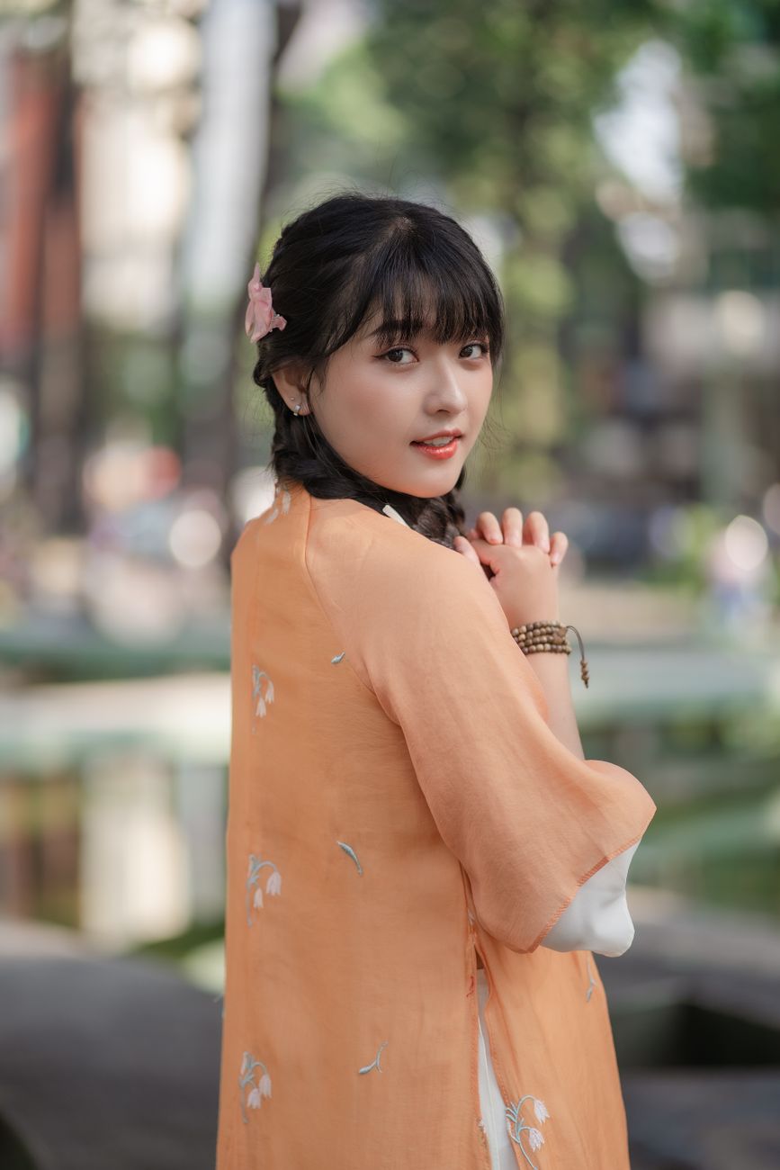 Portrait of a young woman wearing an orange ao dai, posing outdoors with a serene expression.