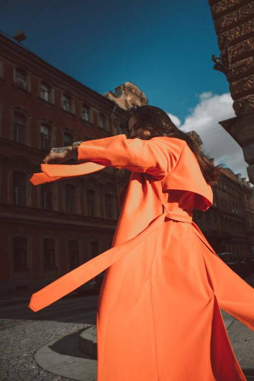 Free Low angle side view of young brunette in long vivid orange coat spinning around in city street with old buildings Stock Photo