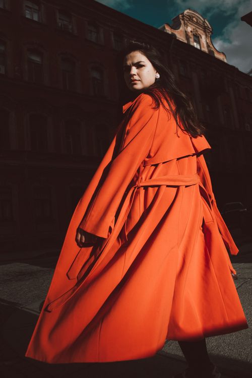Free Fashionable young woman posing in an orange trench coat outdoors during the day. Stock Photo