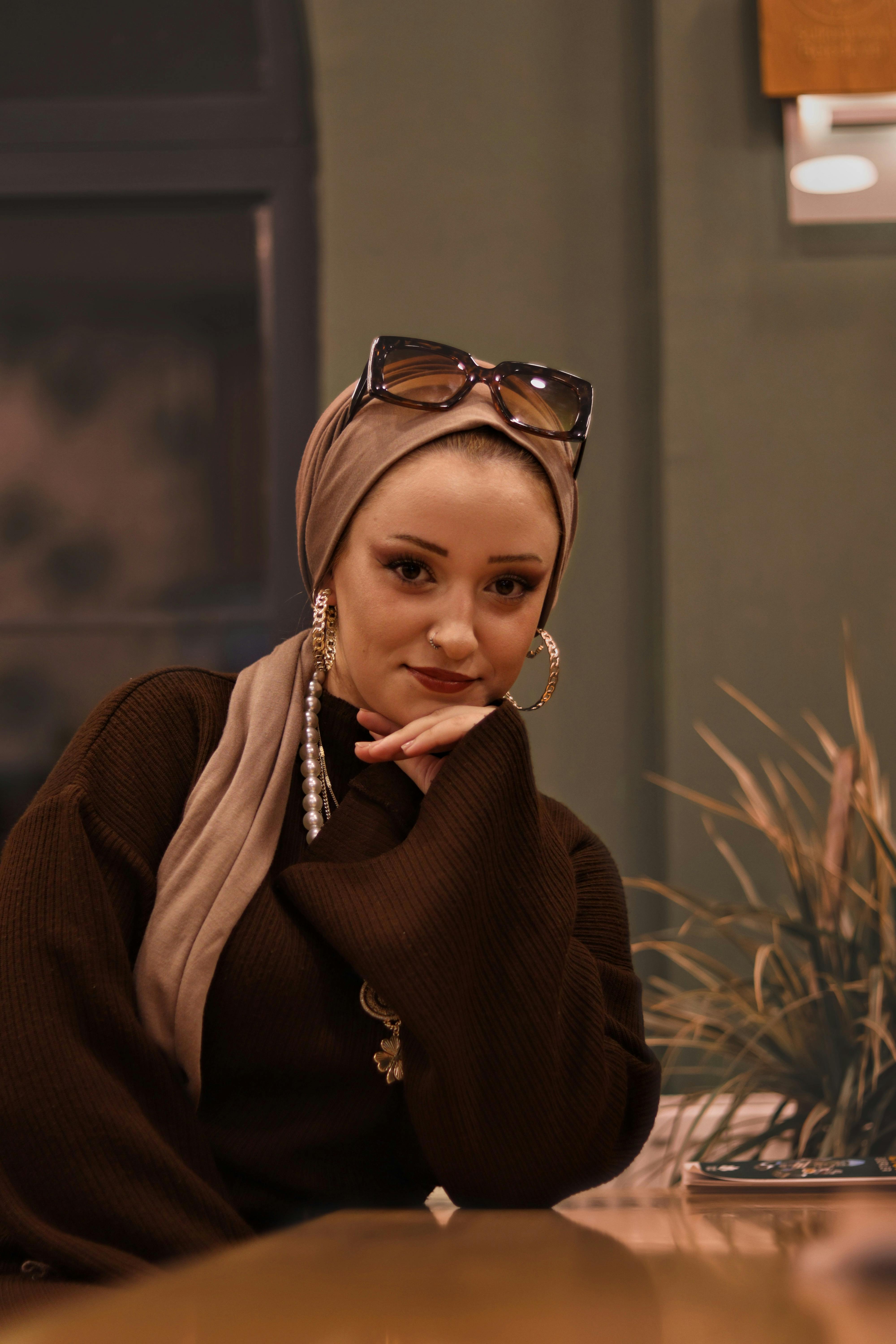 Portrait of a woman in a headscarf with sunglasses sitting in a modern cafe.