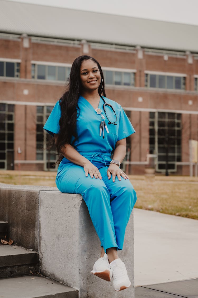 Doctor In Blue Scrubs Sitting In Front Of The Hospital