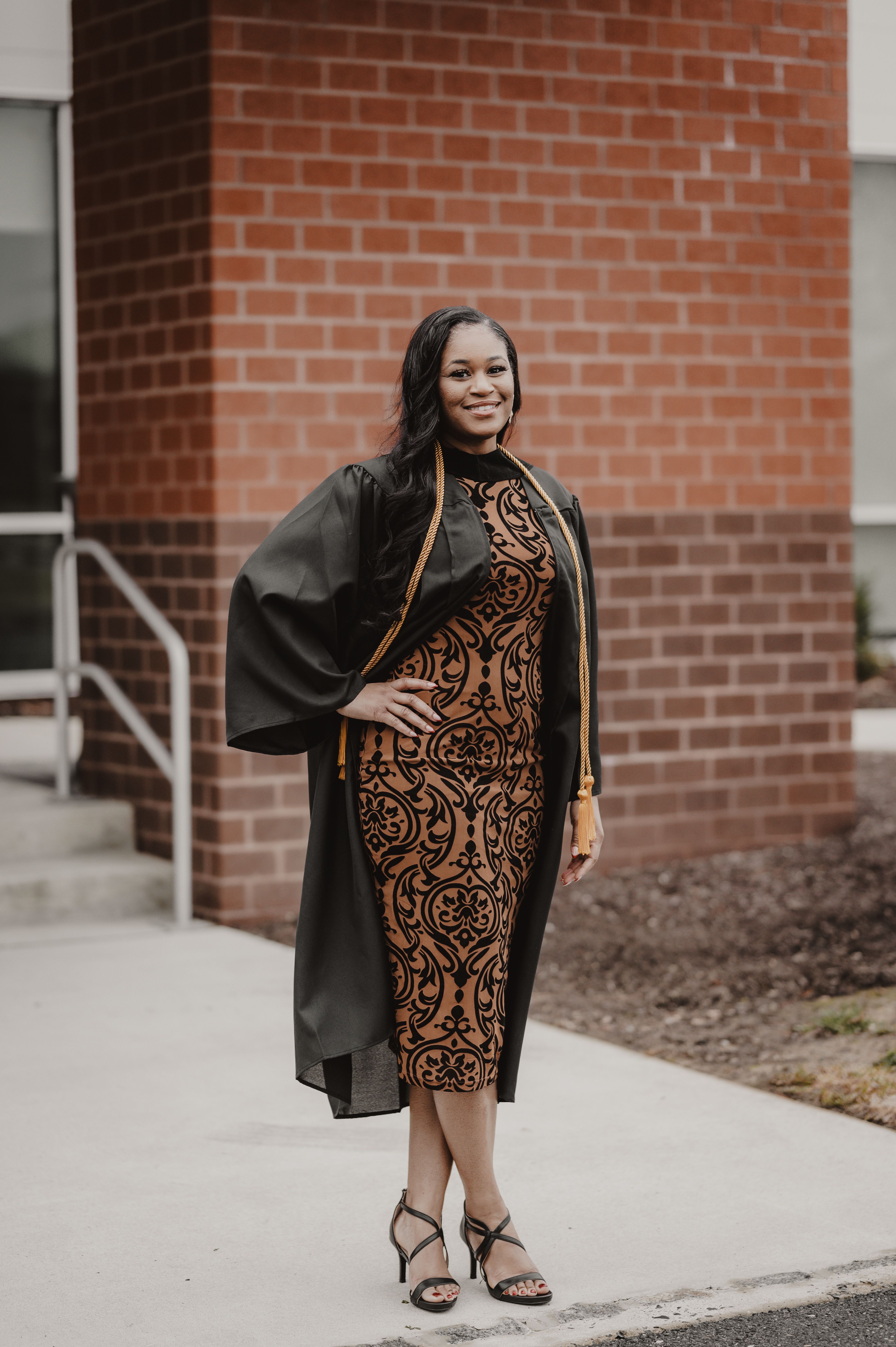 Smiling Woman in Graduate Gown and Brown Dress in Front of a Building   Free Stock Photo