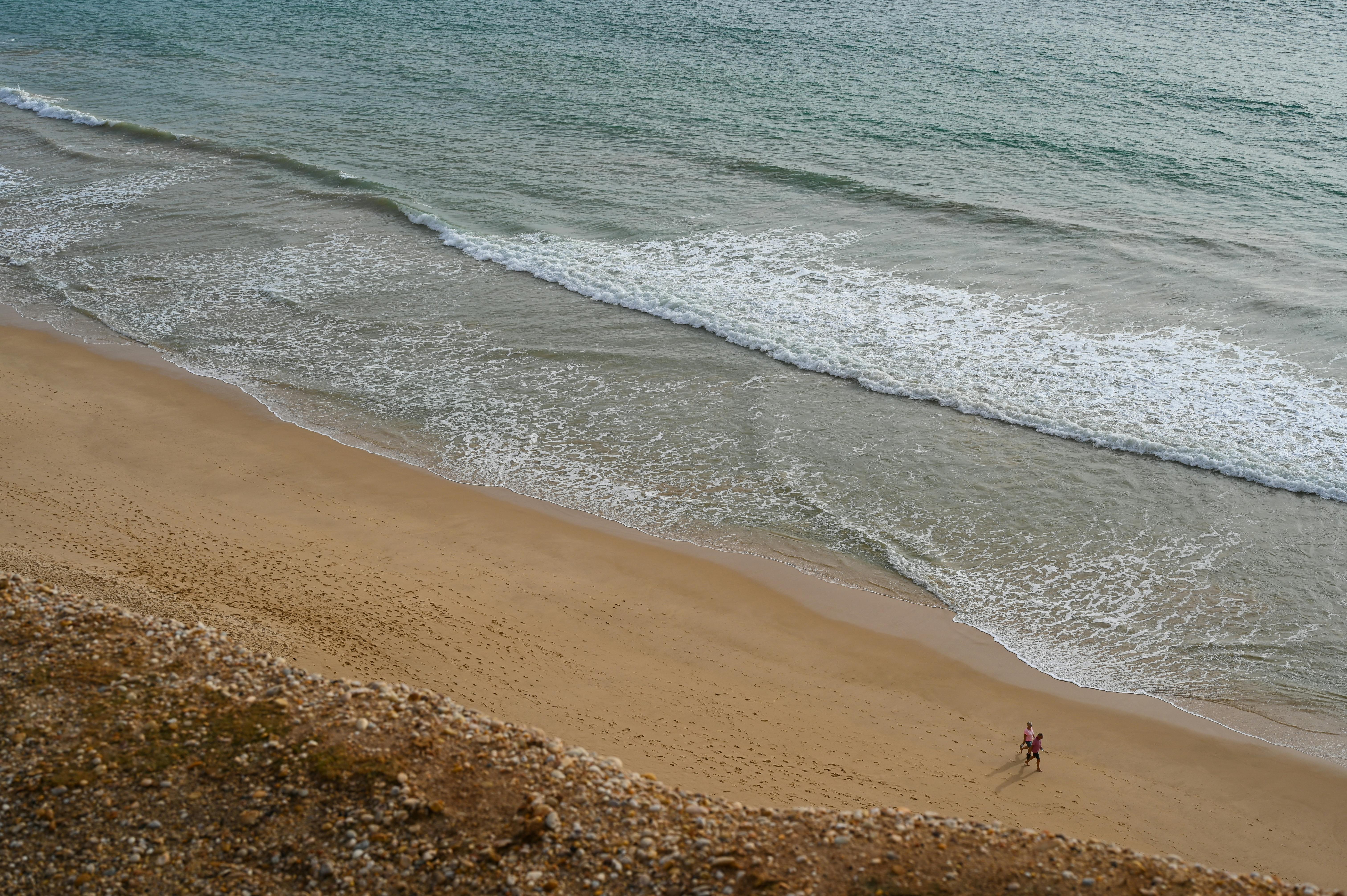 A serene aerial view of Faro beach, capturing waves and the sandy shoreline with two people walking.