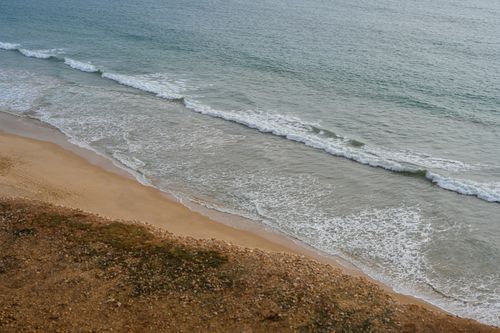 Free Aerial view of the Faro coastline showcasing gentle waves and sandy shores. Stock Photo