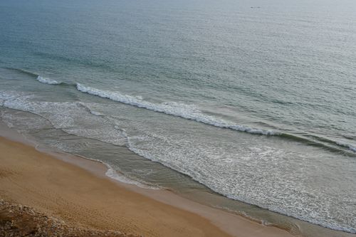Free Serene beach view in Faro, Portugal showcasing waves and sandy shores. Stock Photo