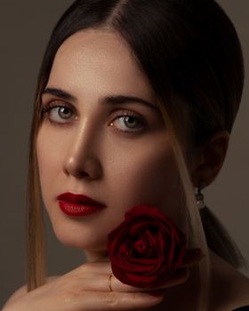 Close-up portrait of a woman holding a red rose, with bold red lipstick and a serene expression.