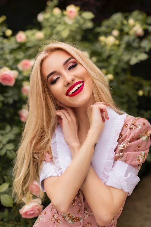 Free Happy woman in a floral dress posing in a vibrant Amsterdam garden with blooming roses. Stock Photo