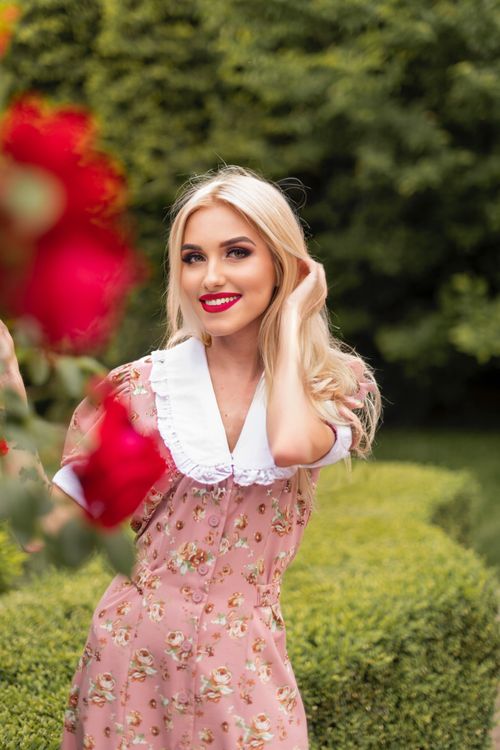 Free A joyful woman with blonde hair enjoying a sunny day in the park surrounded by vibrant flowers. Stock Photo