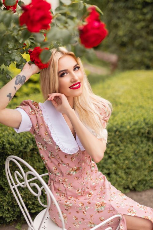 Free Blonde woman in a floral dress sitting amidst roses in Logatec, Slovenia garden. Stock Photo