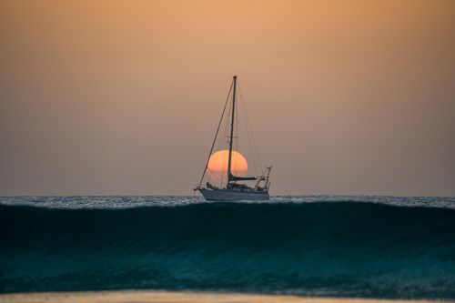 Free A peaceful sailboat glides across the ocean with a stunning sunset backdrop. Stock Photo
