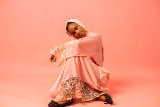 A serene portrait of a woman in pink traditional dress against a soft pink background.