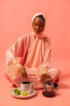 Woman in pink hijab enjoys morning with coffee and citrus fruit.