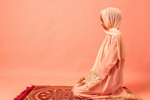 Model in Pink Abaya Robe and Hijab Headscarf Kneeling on a Prayer Rug