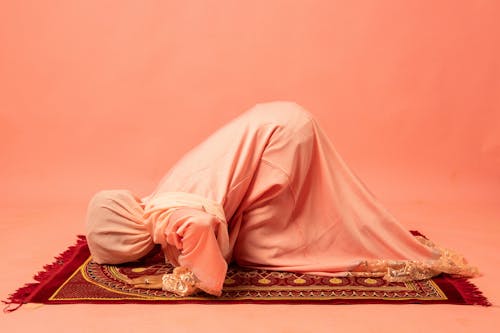 Woman in Pink Abaya and Hijab Prostrating on a Prayer Rug