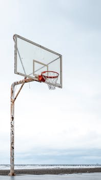 A solitary rusty basketball hoop on a beach, set against a clear sky, evokes a serene and nostalgic mood.