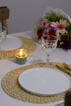 Cozy dinner setup featuring lit candle, floral bouquet, and elegant tableware.