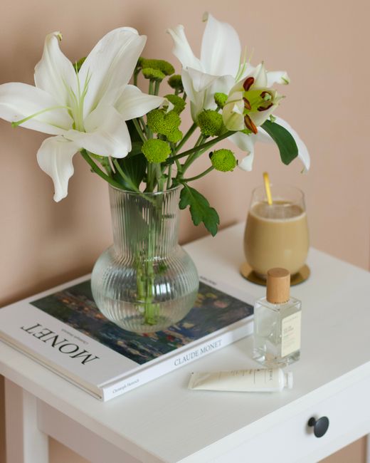 Styled table with white lilies, book, and glass vase creating serene home decor.