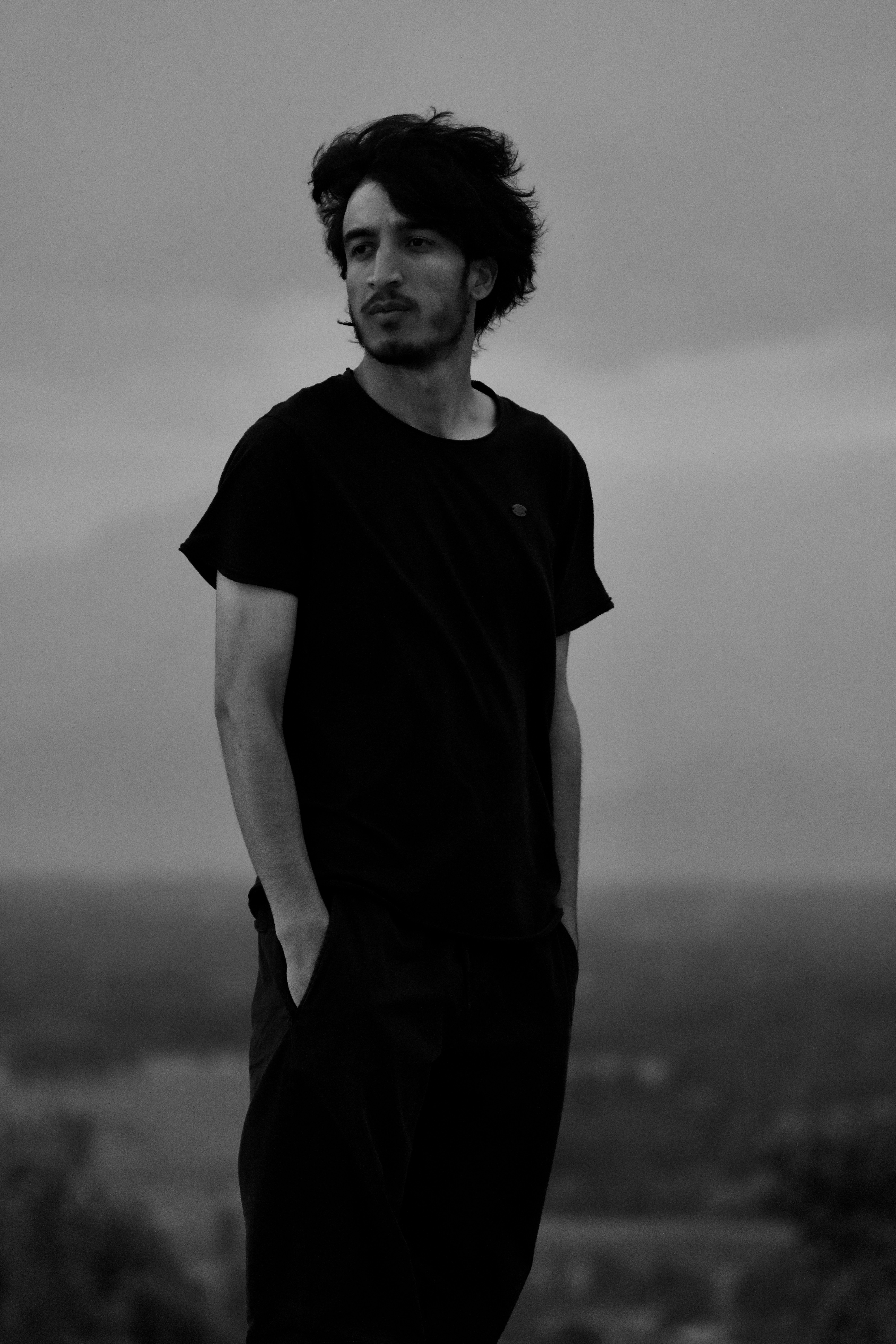 A contemplative man with hands in pockets gazes into the distance in a monochrome setting.
