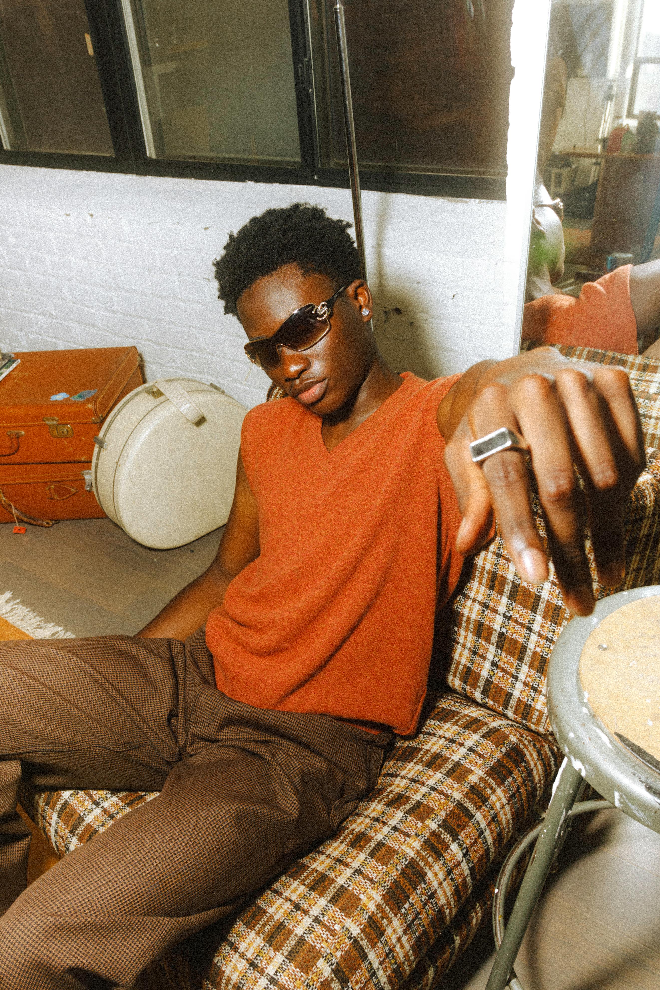 Cool young man in sunglasses seated on a vintage chair indoors in Toronto.