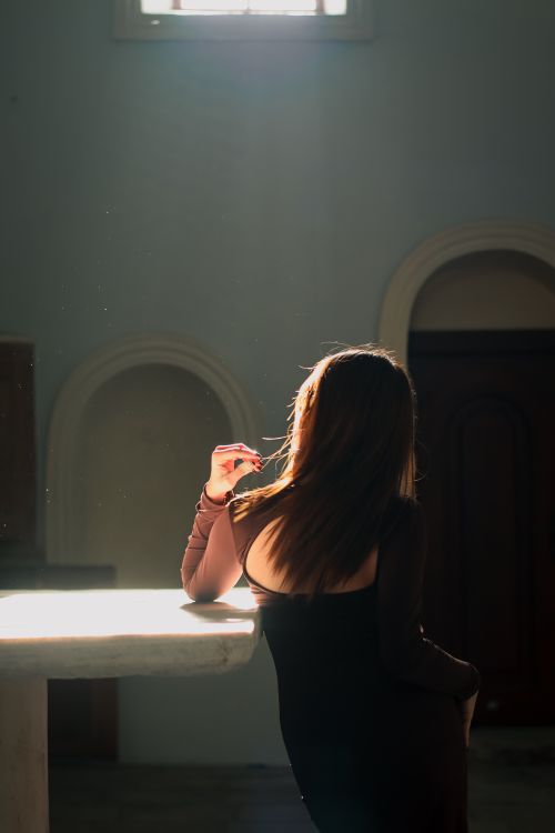 Free A woman leans on a table bathed in sunlight, creating a serene and introspective mood. Stock Photo
