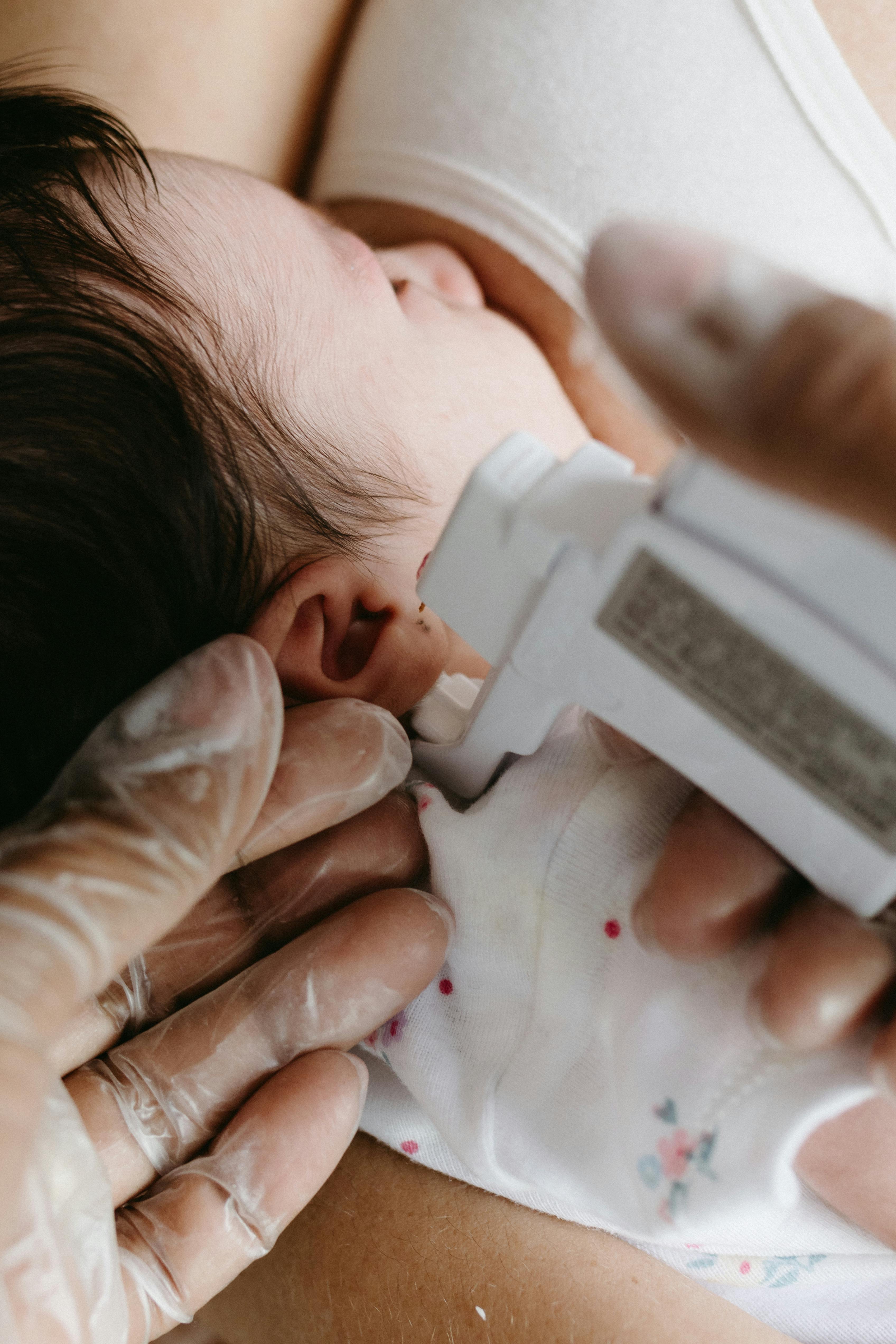 Close-up of a newborn receiving ear care with gentle hands in a healthcare setting.