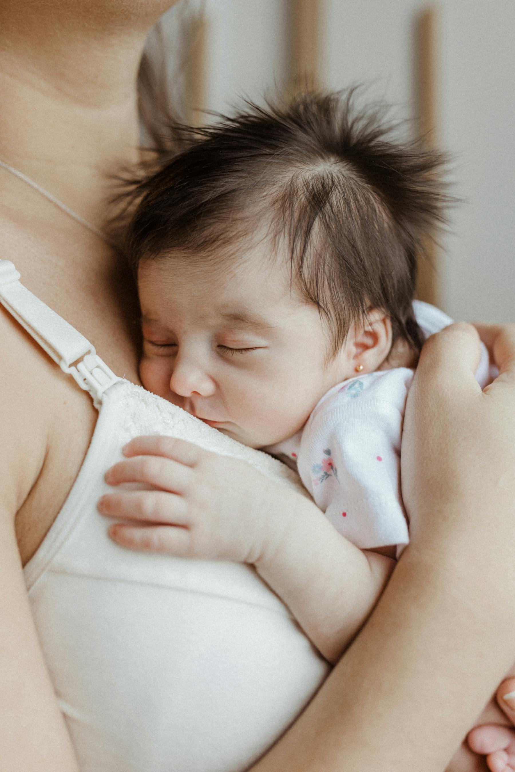 A mother holding her sleeping newborn with quiet tenderness
