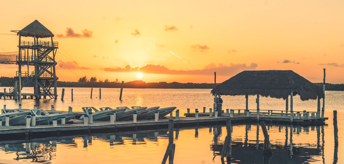 Timber jetty and thatched deck over calm water at sunset — Vechoor, Kottayam, representative image
