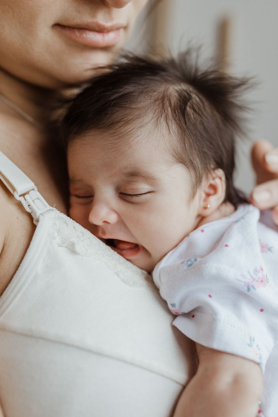 Mother tenderly holding her newborn baby against her chest indoors