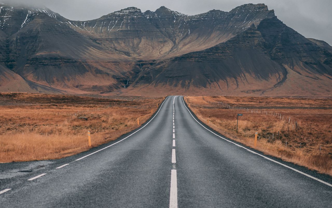 Empty highway stretching toward snow-capped peaks under dark moody skies