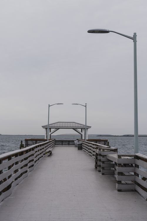 Free A tranquil overcast view of a wooden pier stretching into the ocean with a gazebo at the end. Stock Photo
