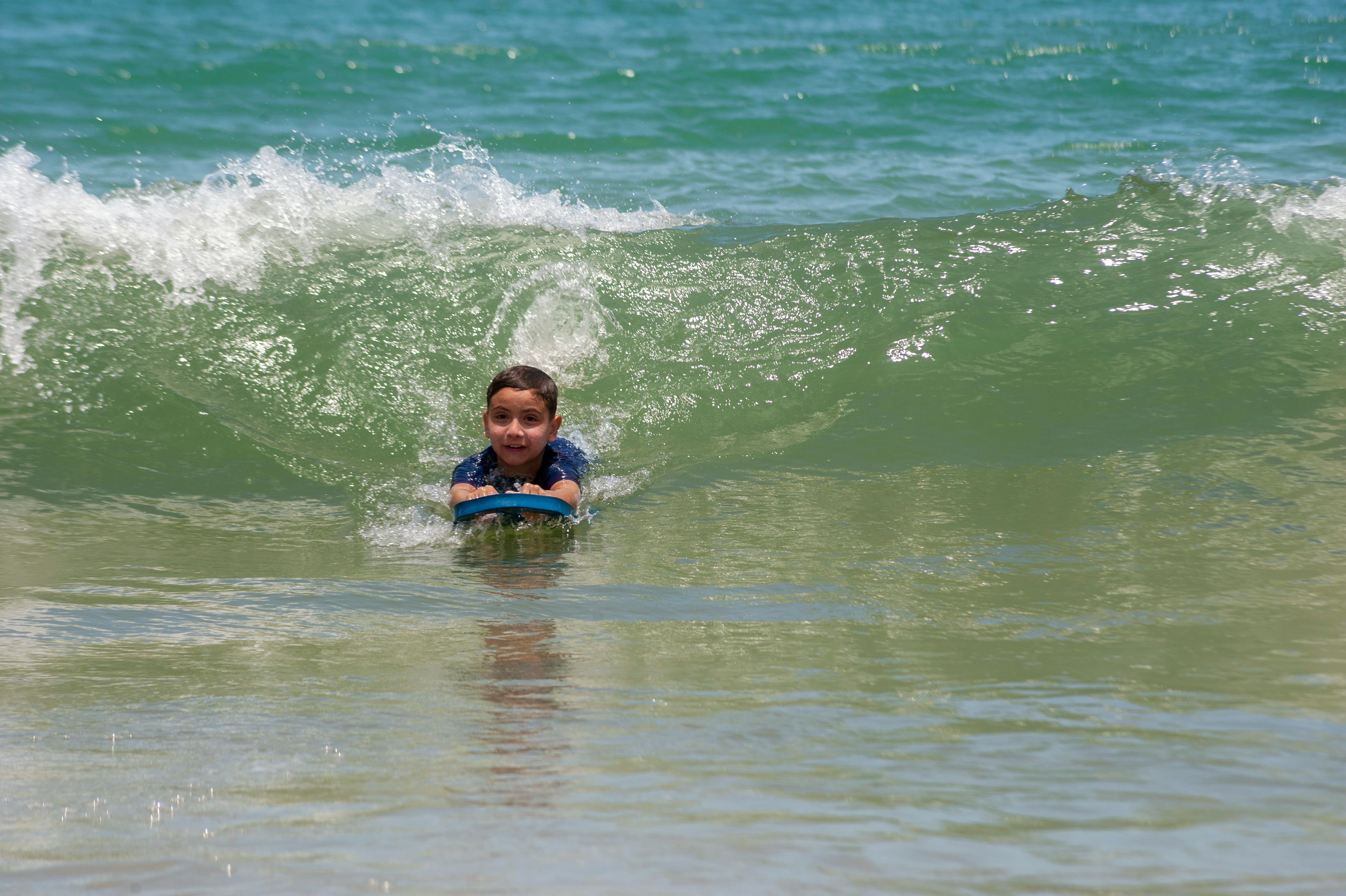 Young bodyboarder riding a small shore-break wave on a sandy beach