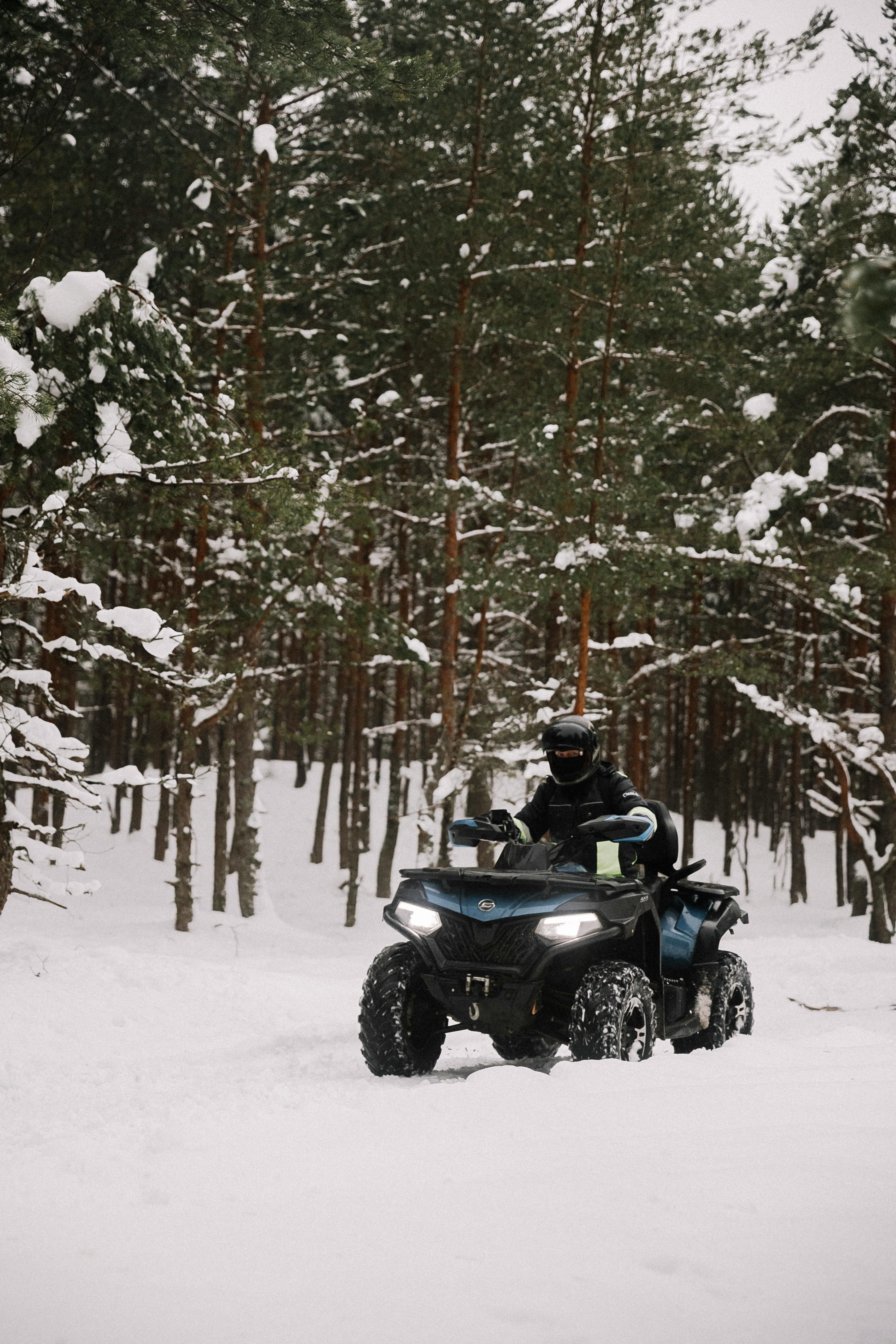 A person riding an ATV through a snow-covered forest during winter, showcasing outdoor adventure and winter sports.