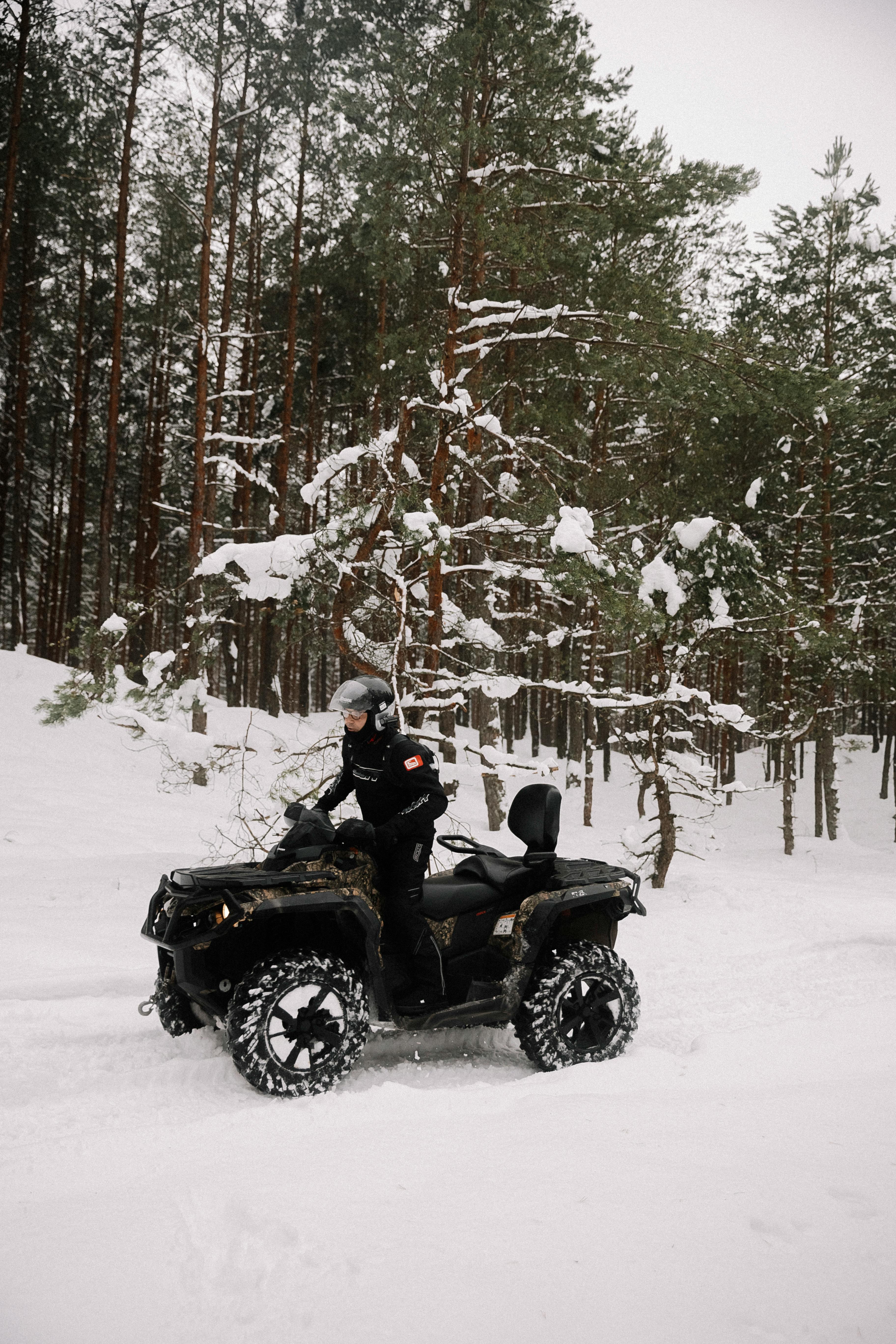 Man riding an ATV through snowy forest landscape in wintertime.