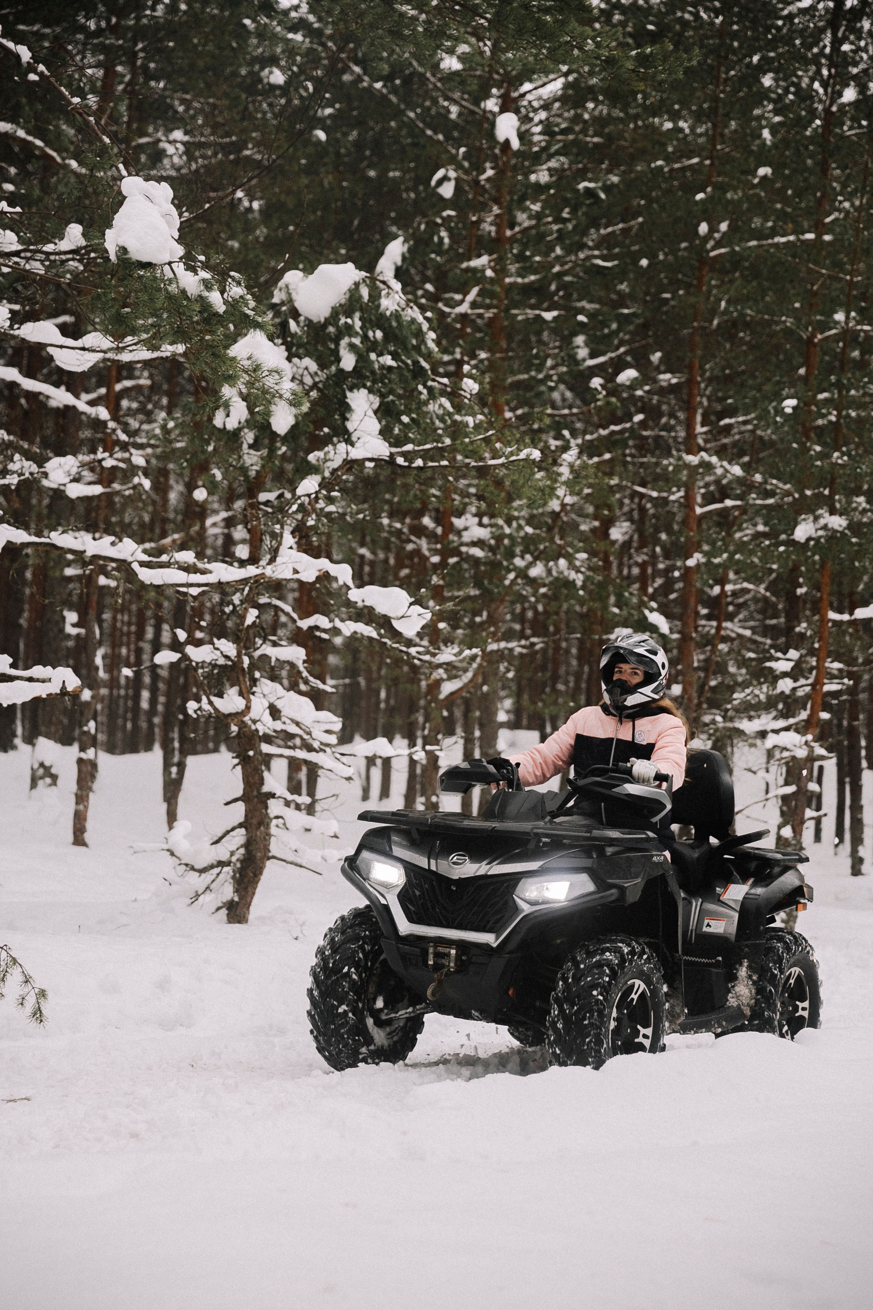 Person riding an ATV through a snowy forest, showcasing winter adventure and transportation.