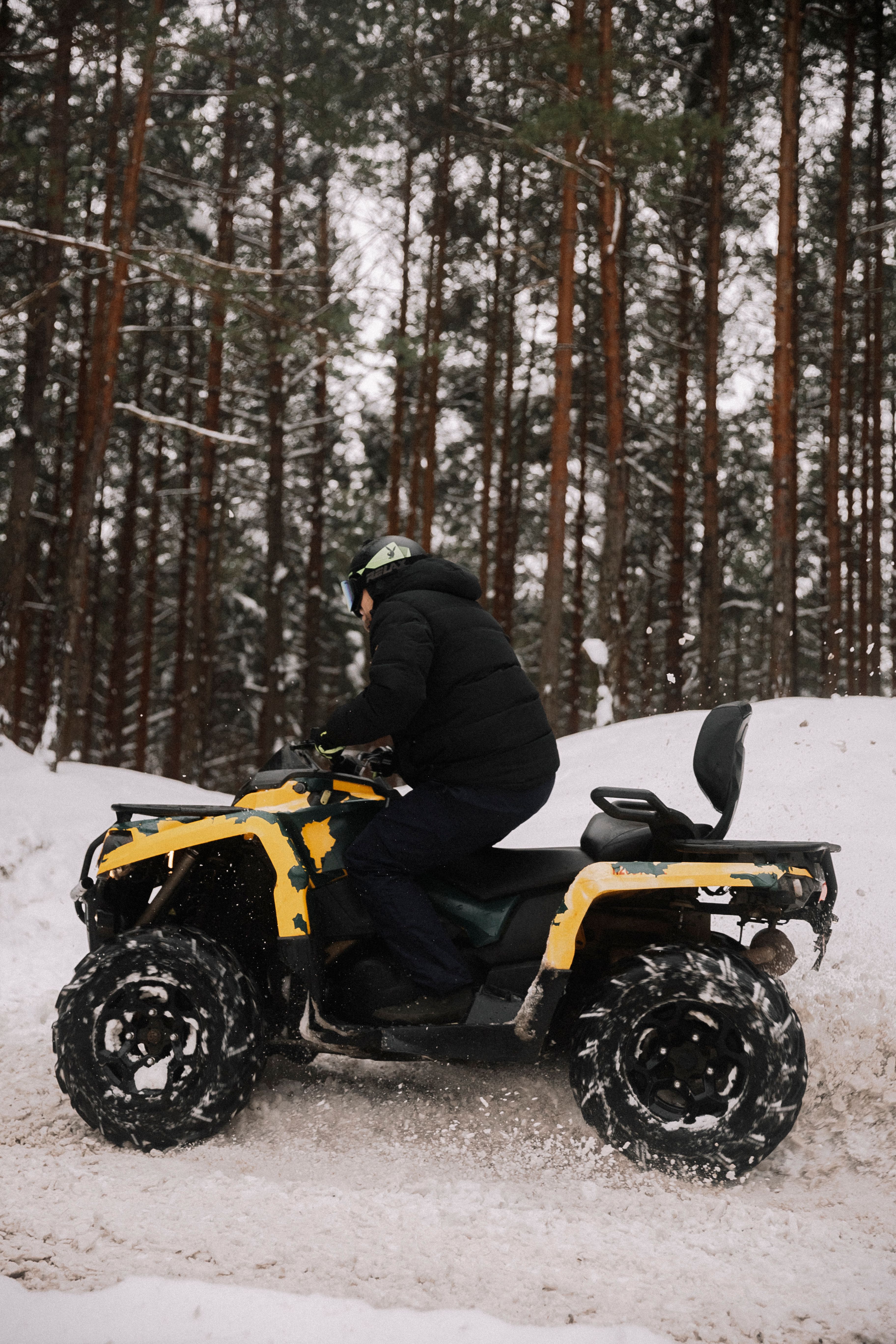 A person riding an ATV through a snowy forest, showcasing winter adventure and outdoor exploration.