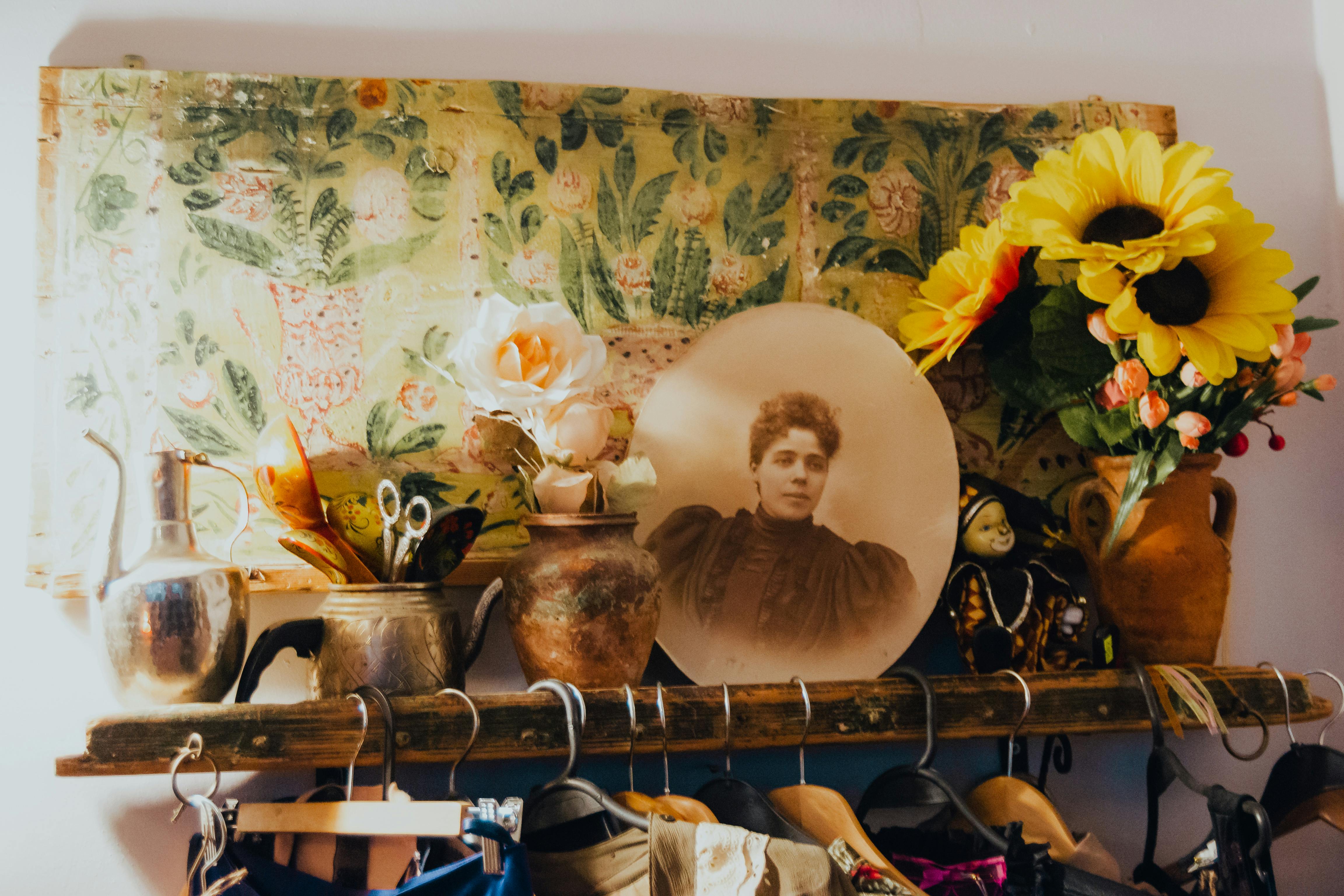 A vintage shelf displaying sunflowers, vases, and a vintage portrait against floral wallpaper.