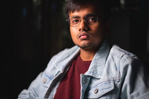 Free Stylish portrait of a young man wearing glasses and a jean jacket, set against a dark background. Stock Photo