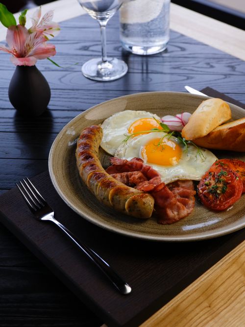 Free Delicious gourmet breakfast featuring fried eggs, sausage, bacon, and toast served elegantly on a plate. Stock Photo