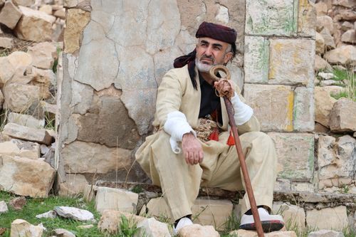 Free Elderly man with beard resting in desert ruins, wearing traditional attire and holding a cane. Stock Photo
