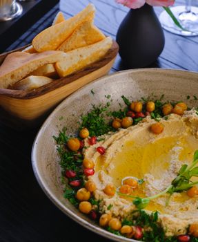 A bowl of creamy hummus garnished with chickpeas, herbs, and pomegranate seeds next to bread slices.