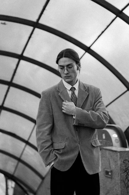Black and white photo of a man in a suit standing in an urban tunnel station.