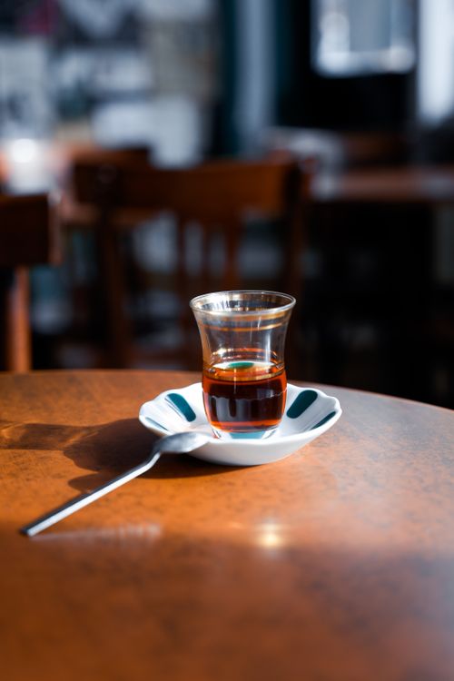 Free A steaming glass of tea on a plate with a spoon in a cozy, dimly lit café. Stock Photo