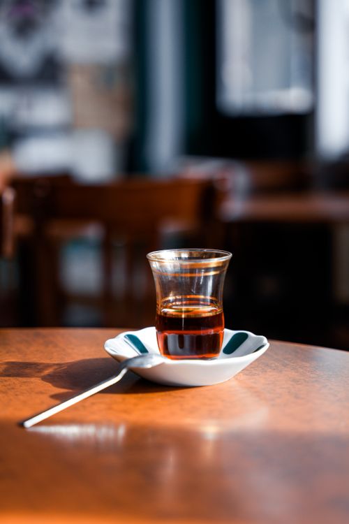 Free Turkish tea in traditional glass with saucer on a sunlit wooden table inside a café. Stock Photo