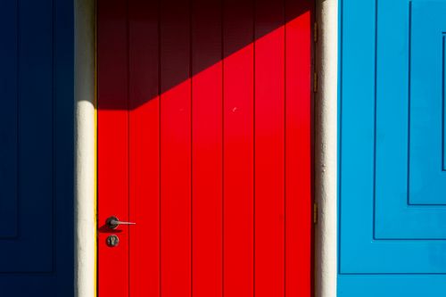 Free A striking red door set against a vivid blue wall, featuring modern design and bold colors. Stock Photo