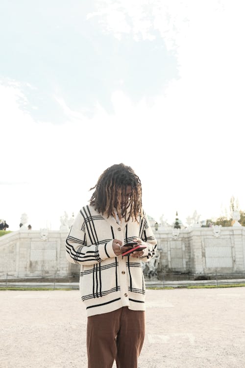 A Man with Dreadlocks Wearing a Sweater Using His Phone Outside 