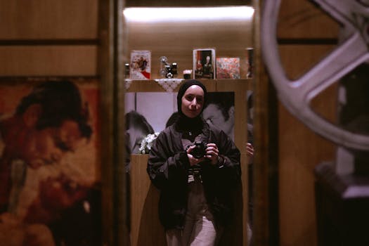 Portrait of a young woman in hijab holding a camera in a retro-themed room.