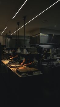 Chefs are carefully preparing food in a dimly lit professional kitchen, showcasing a collaborative cooking environment.